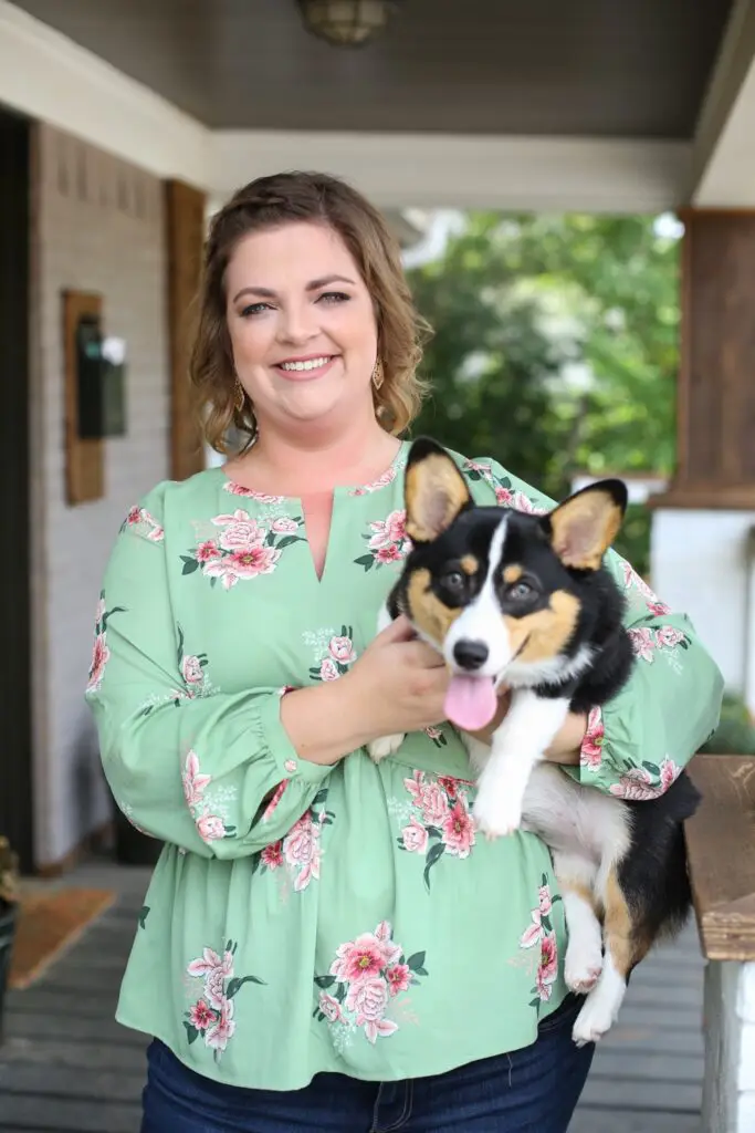 Hailey wearing a green shirt with pink flowers and holding a tri-colored corgi