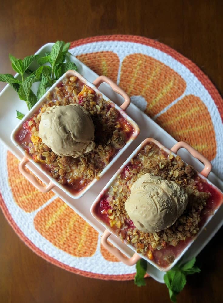 two small square dishes filled with peach raspberry crumble topped with a scoop of ice cream