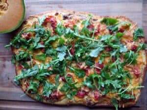 a rectangular shaped pizza with cooked meat and an abundance of fresh greens