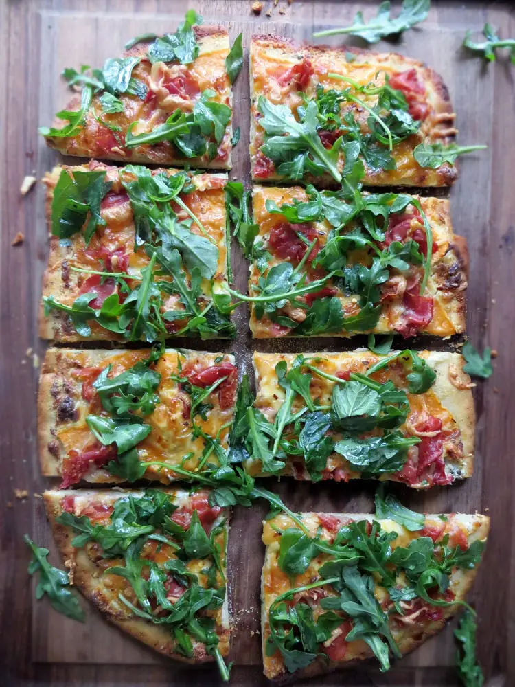 eight rectangular slices of pizza garnished with fresh greens and pieces of thinly sliced prosciutto
