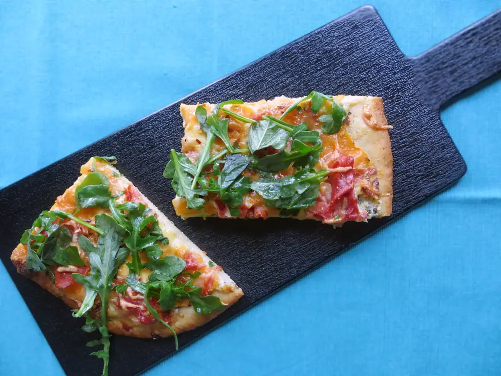 a black board holding two rectangular slices of pizza topped with fresh green arugula