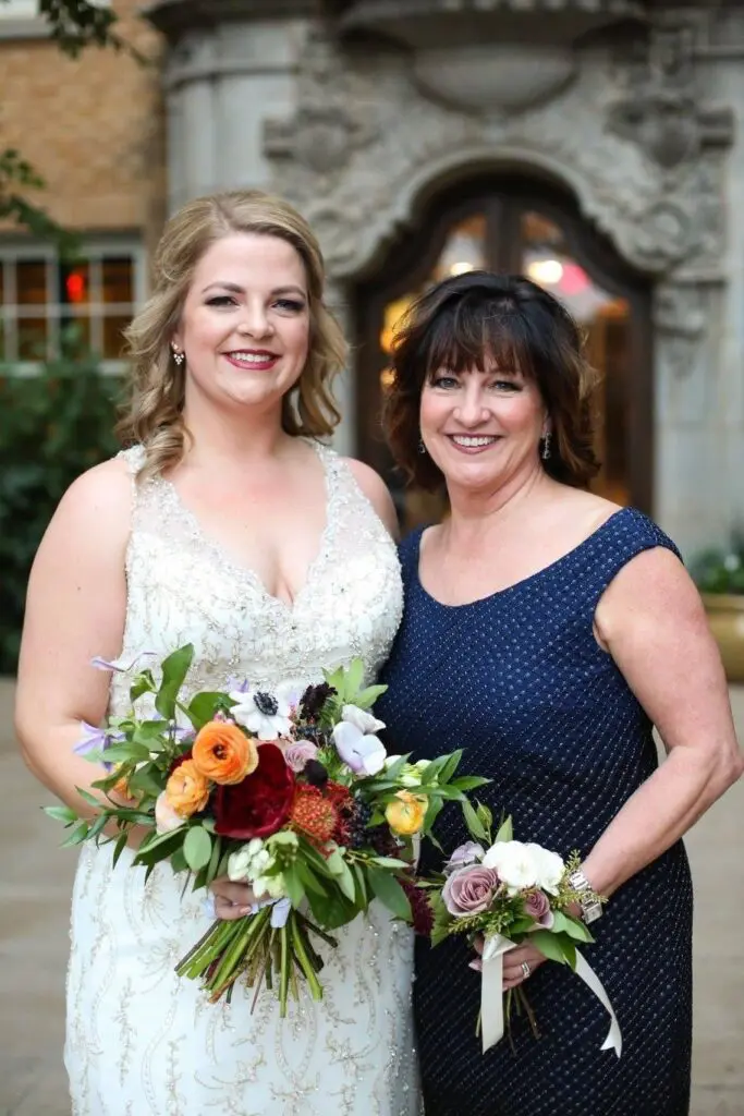 Two adult women, one in a wedding dress holding a bouquet and the other in a navy dress