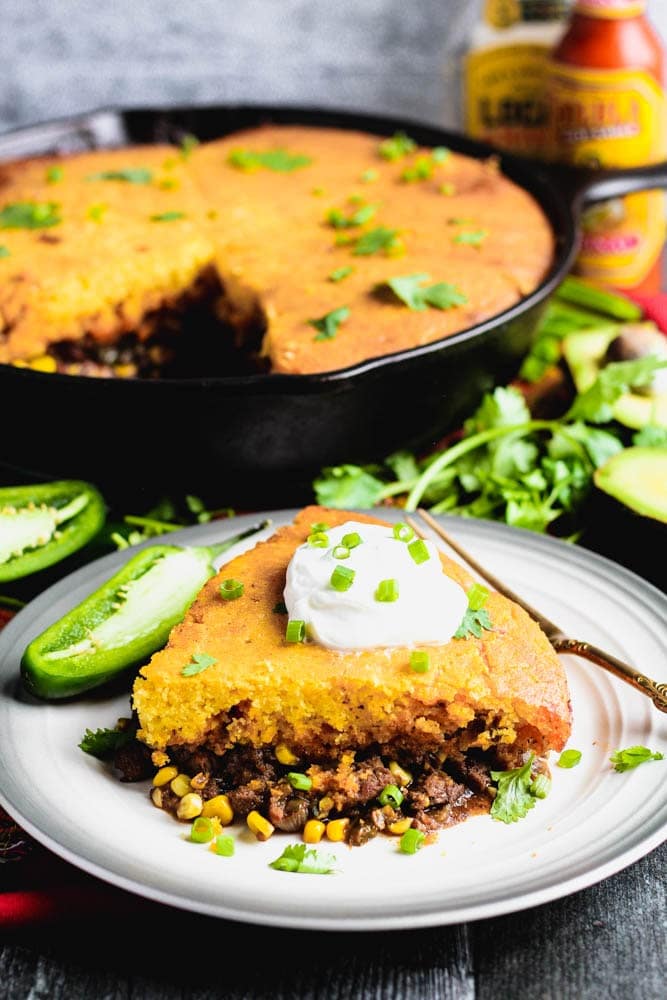 a portion of taco cornbread pie garnished with sour cream and sliced green onions on a round plate