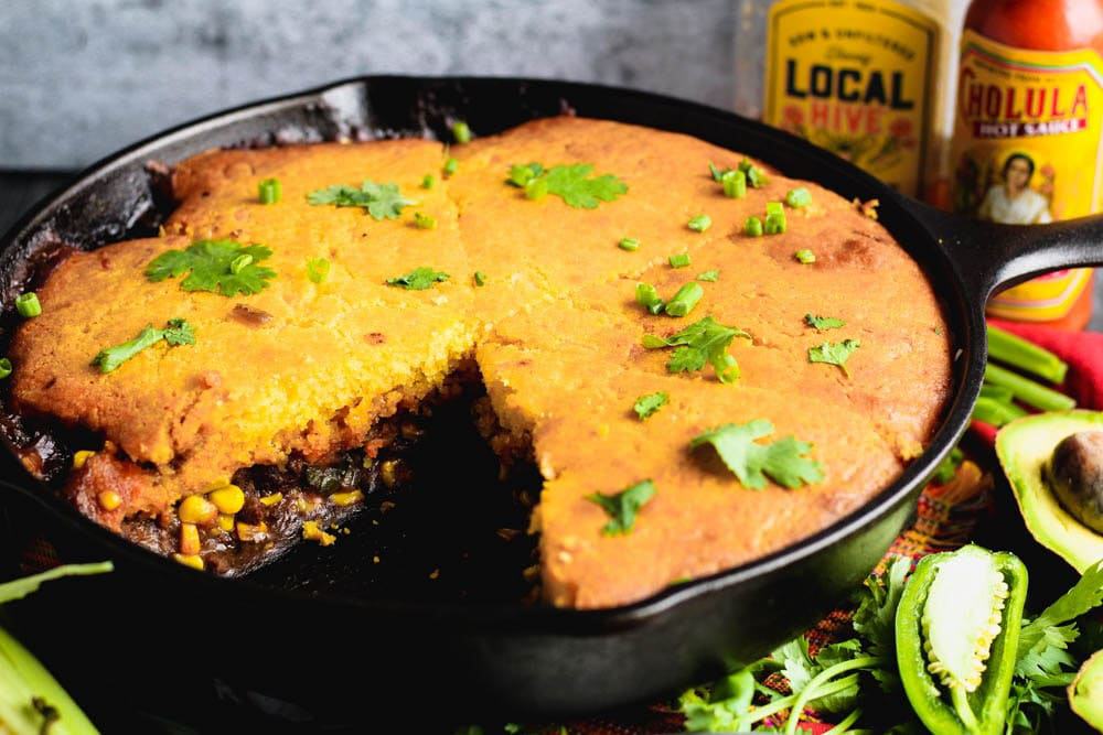 cornbread over meat and corn in a cast iron skillet