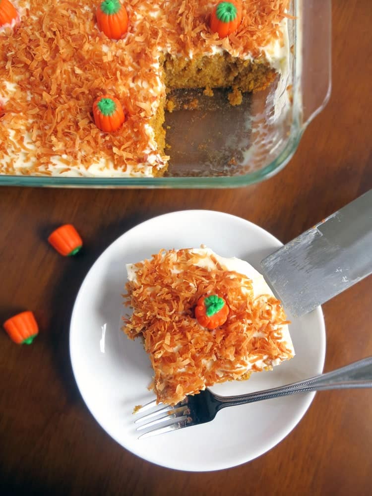 a slice of cake topped with white frosting and orange coconut flakes on a small white plate