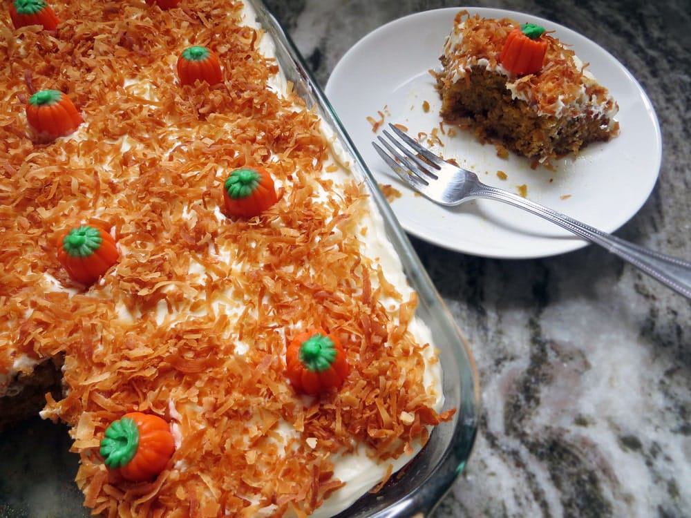 a cake topped with white frosting, orange colored coconut flakes, and mini pumpkin candies in a glass baking dish