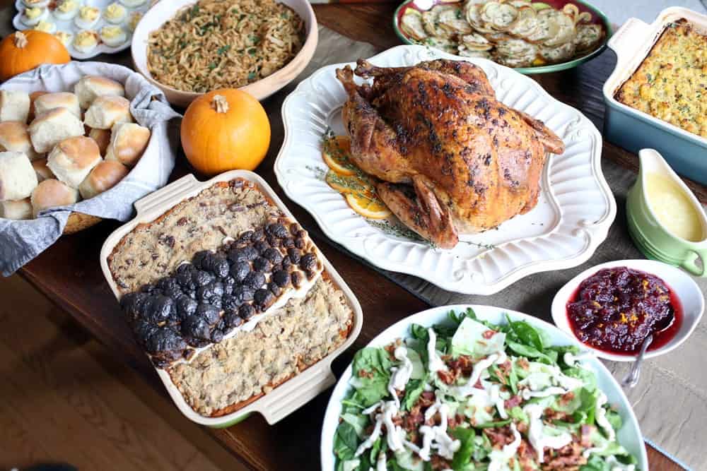 a cooked turkey on a platter surrounded by different side dishes on a wooden table