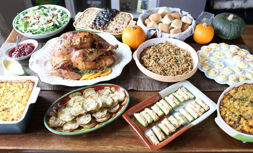 nine Thanksgiving dishes arranged on a wooden table decorated with small pumpkins