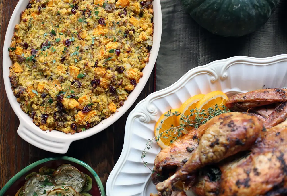 cornbread sausage dressing in an oval baking dish beside a cooked turkey on a white platter