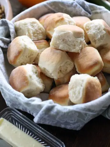 homemade dinner rolls in a bowl lined with a cloth towel