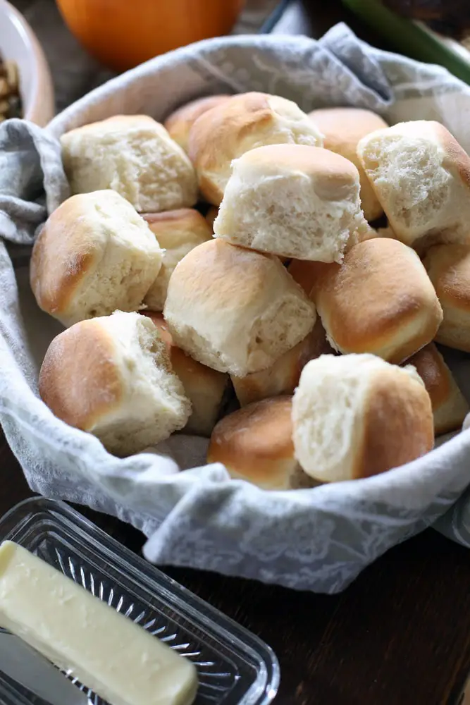 homemade dinner rolls in a bowl lined with a cloth towel