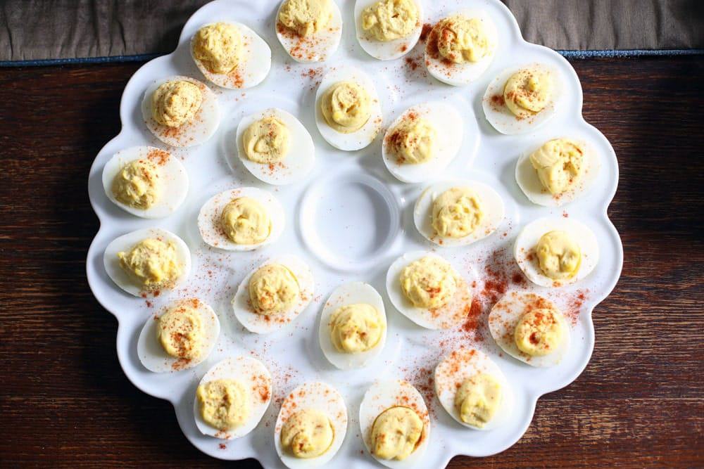 deviled eggs garnished with paprika on a fluted white serving tray