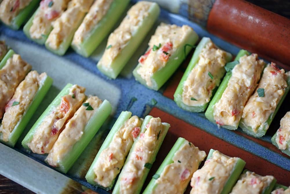 a platter lined with sticks of celery filled with creamy yellow cheese filling