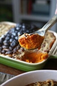 a metal spoon scooping a portion of sweet potato casserole from a baking dish