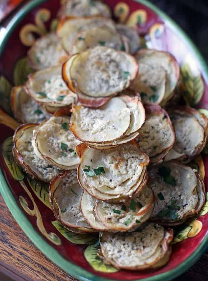 thinly-sliced rounds of potato stacks on an ornate red and green oval platter