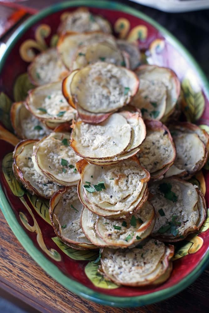 thinly-sliced rounds of potato stacks on an ornate red and green oval platter