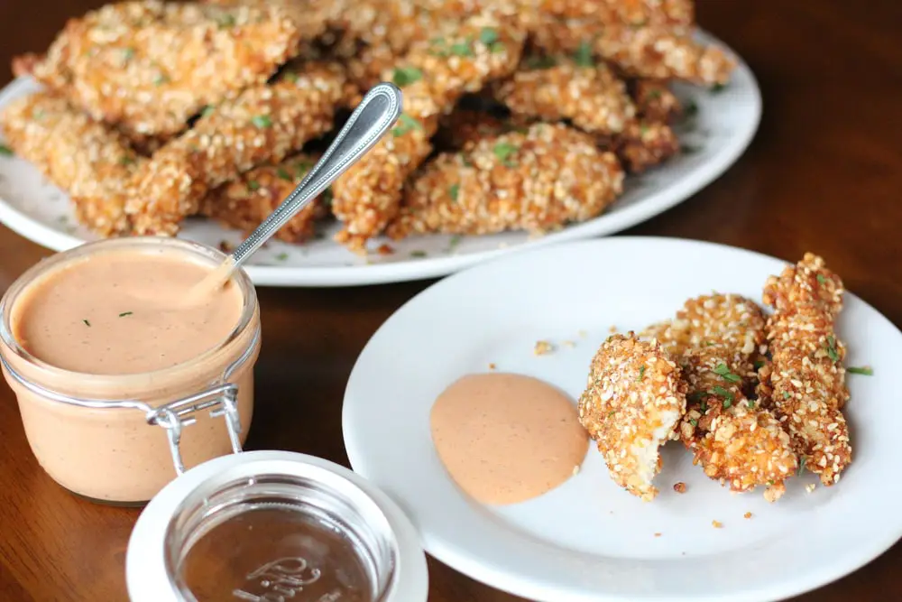 chicken tenders on a round white plate served with an orange creamy sauce