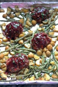a pan of individual barbecue topped meatloaves with roasted string beans and potatoes on
