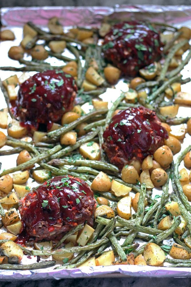 a pan of individual barbecue topped meatloaves with roasted string beans and potatoes on