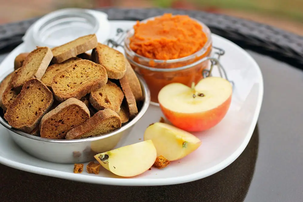 a bowl of baked dog biscuits on a plate with sliced apple and a jar of pumpkin puree