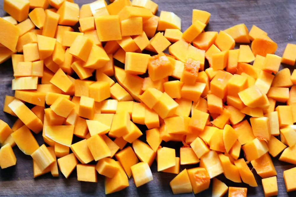 cubes of orange butternut squash piled on a wood cutting board