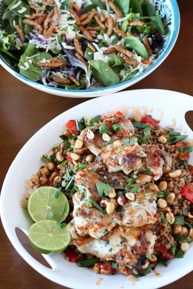 Tahini Chicken with Crispy Farro in a white serving bowl beside a bowl filled with an asian slaw and greens salad sprinkled with sesame sticks