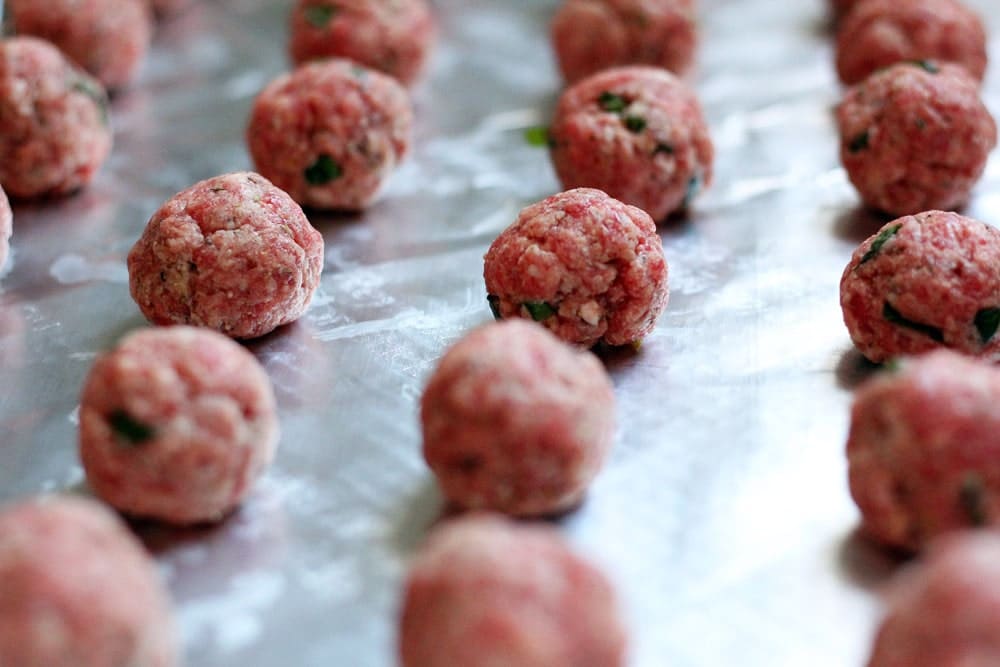 unbaked meatballs with bits of green on a baking sheet lined with aluminum foil