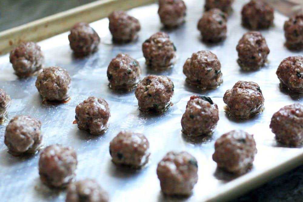 rows of baked meatballs line an aluminum foil-lined metal baking sheet