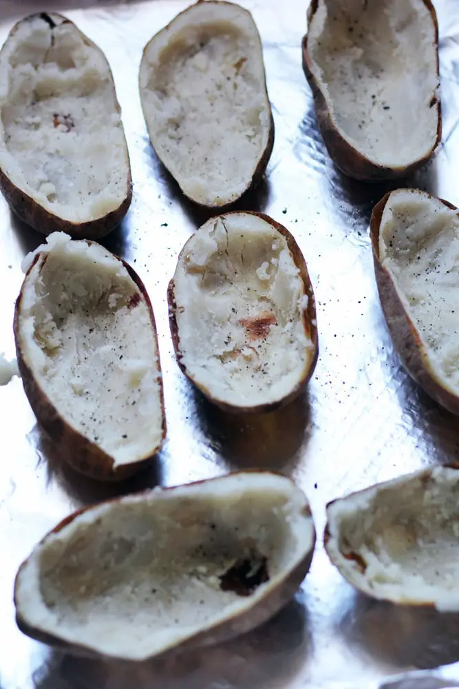 rows of baked potatoes with most of the flesh scooped out on a metal baking sheet