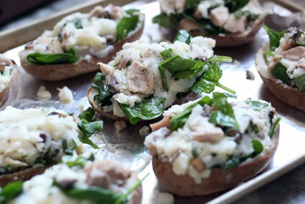 baked potato halves stuffed with a mixture of spinach, chicken, potato, and cheese on a baking sheet ready for the oven