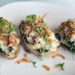 three baked potatoes stuffed and topped with French fried onions and thinly cut green herbs