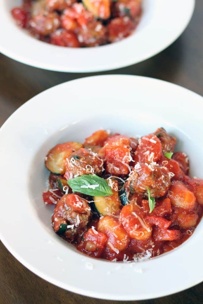 gnocchi with meatballs in a red sauce garnished with grated Parmesan cheese and basil leaves in white bowls