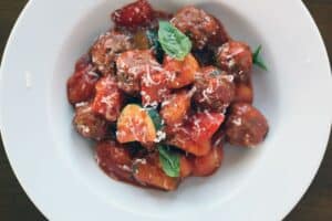 a mixture of potato gnocchi, sliced zucchini and small meatballs covered in red sauce in a round white bowl