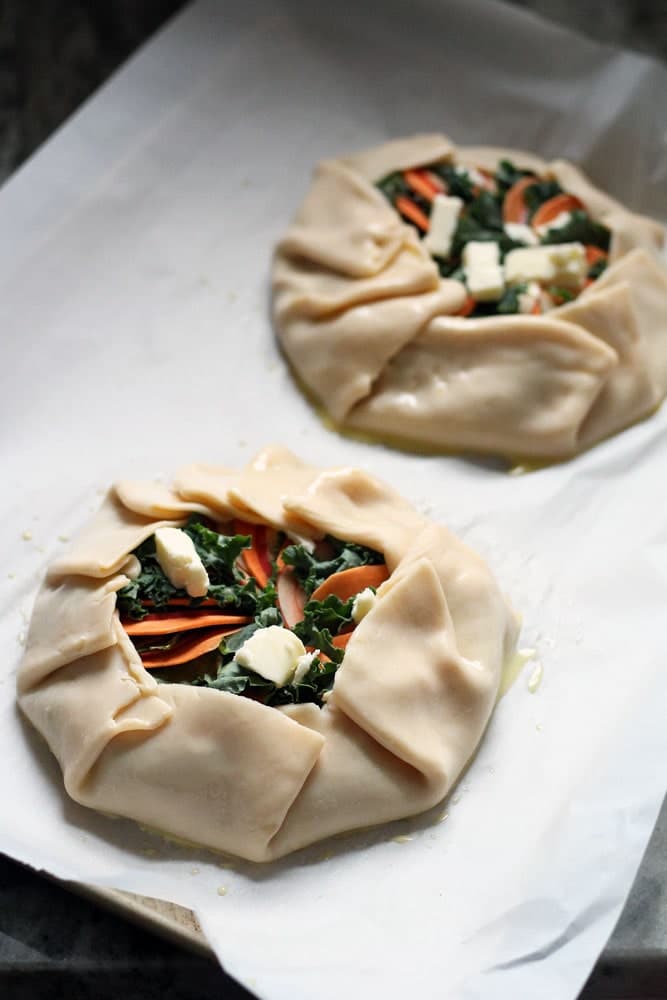two unbaked galette pastries filled with orange and green vegetables on a baking sheet
