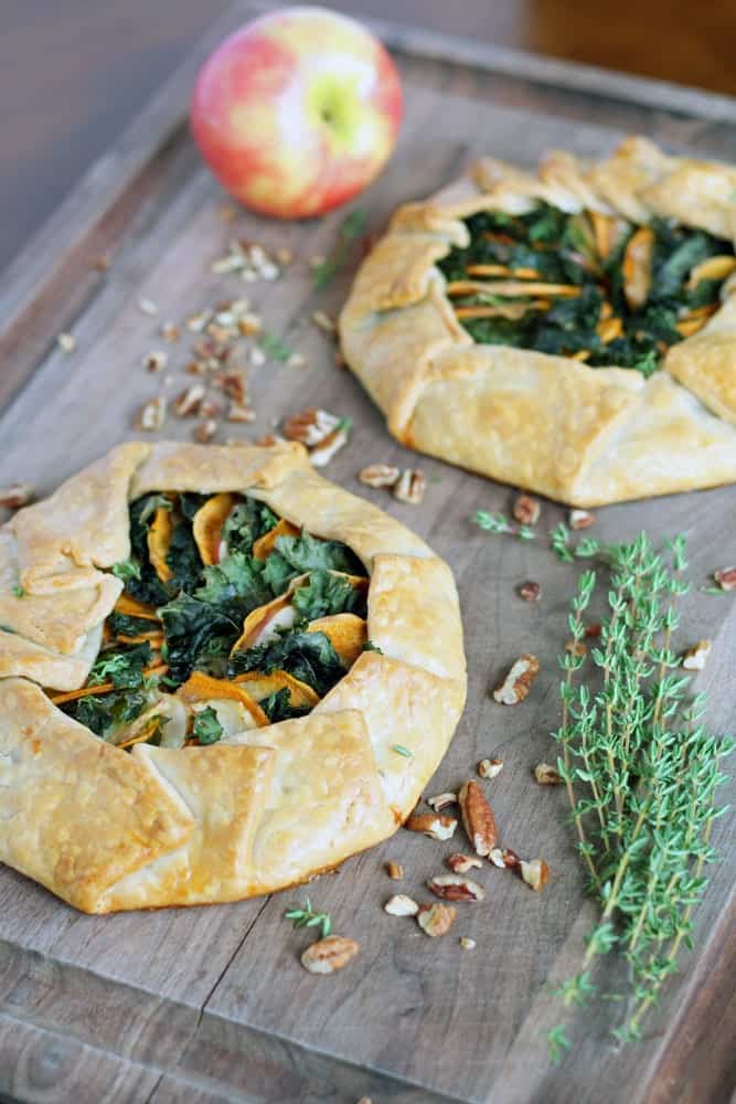 two round baked pastries filled with leafy greens and thinly sliced sweet potato on a cutting board