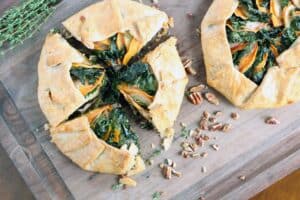 a sweet potato apple and kale galette cut into four wedges aside an uncut galette of the same variety