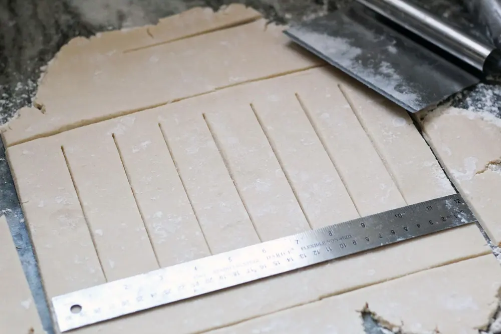 a sheet of pastry dough scored into strips measured by a metal ruler laying on the dough