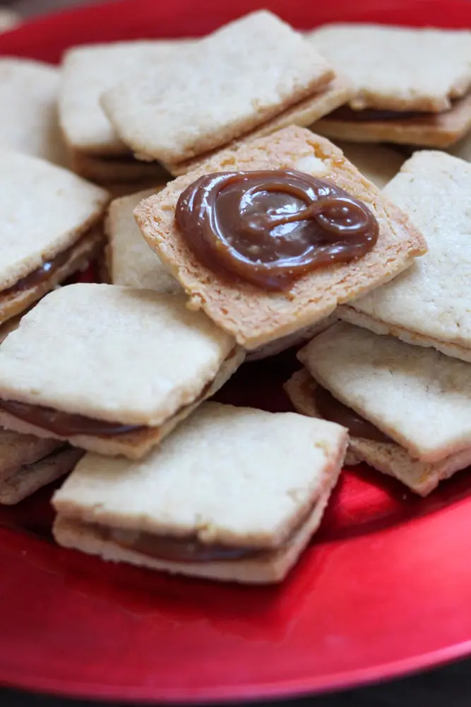 shortbread sandwich cookies filled with caramel on a round red plate