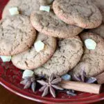 a red plate stacked with brown cookies garnished with candied ginger, star anise, and cinnamon sticks