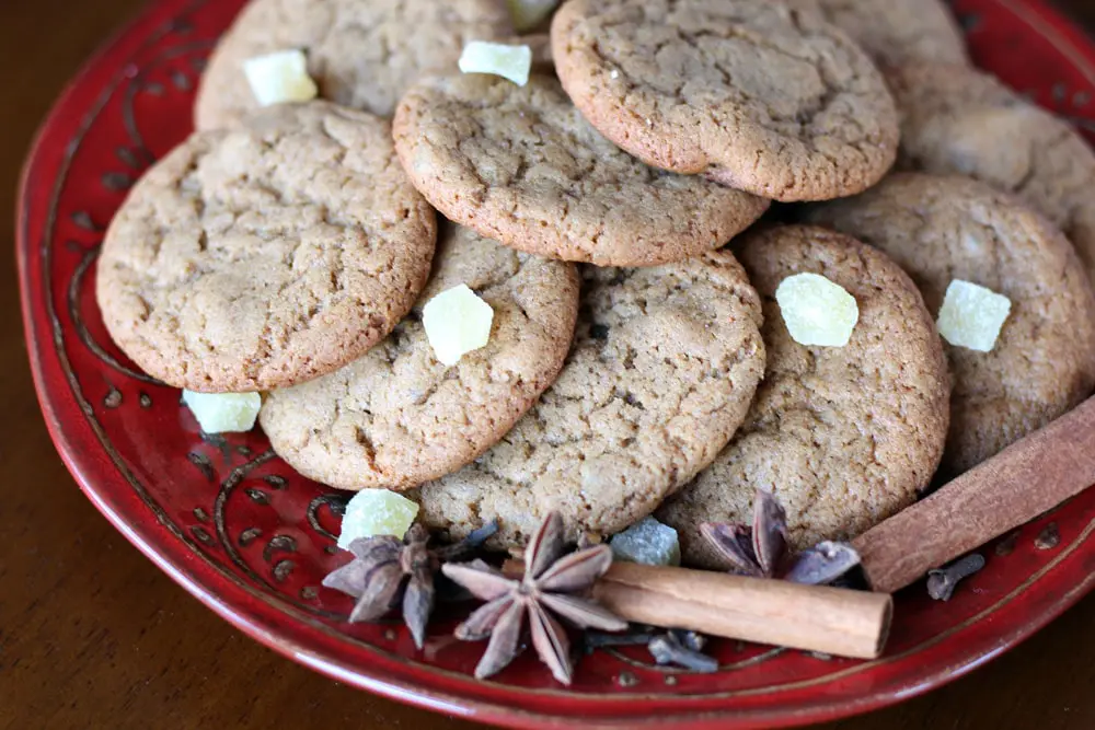 a red plate stacked with brown cookies garnished with candied ginger, star anise, and cinnamon sticks