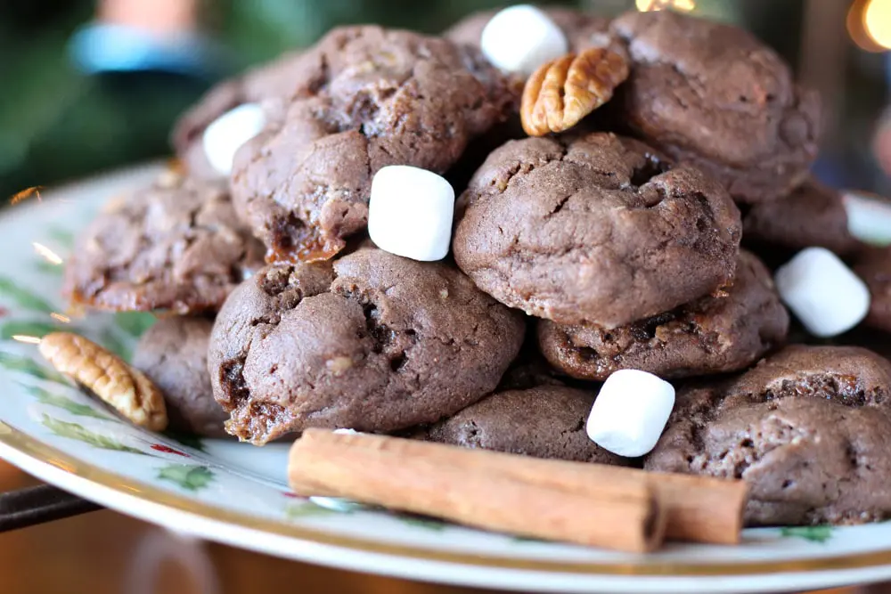 chocolate cookies on a christmas patterned plate garnished with marshmallows and pecans