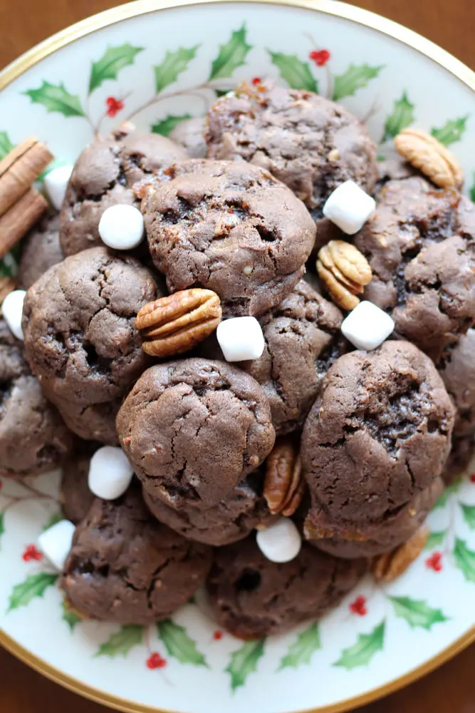 chocolate cookies on a christmas patterned plate garnished with marshmallows and pecans