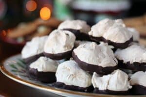 a holly & ivy patterned gold rimmed plate piled with meringue cookies dipped in chocolate