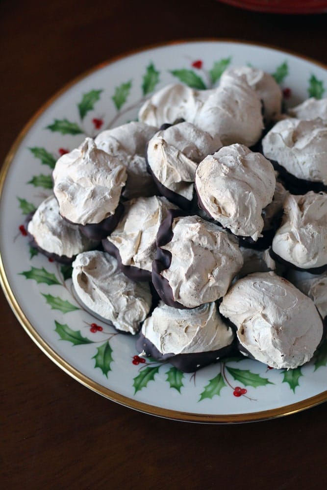 a holly & ivy patterned gold rimmed plate piled with meringue cookies dipped in chocolate