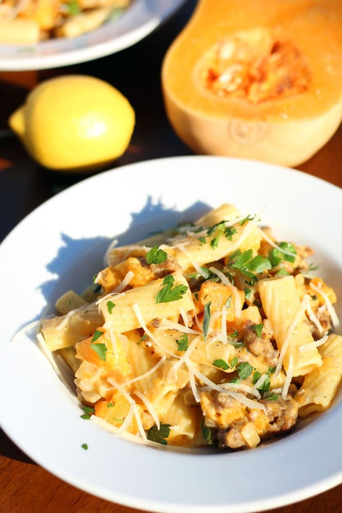 a bowl filled with a mixture of rigatoni pasta, ground sausage, and butternut squash