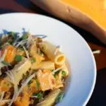 a bowl filled with a mixture of rigatoni pasta, ground sausage, and butternut squash