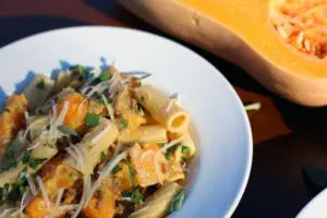 a bowl filled with a mixture of rigatoni pasta, ground sausage, and butternut squash