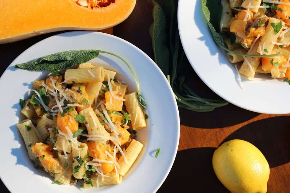 sausage and butternut squash rigatoni served in white bowls and topped with white shredded cheese and chopped green herbs
