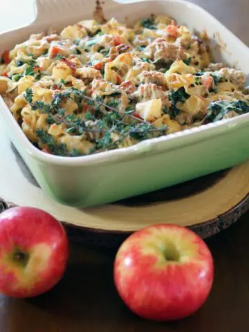 a square baking dish filled with a mixture of diced apple, pork, and spinach topped with melted cheese