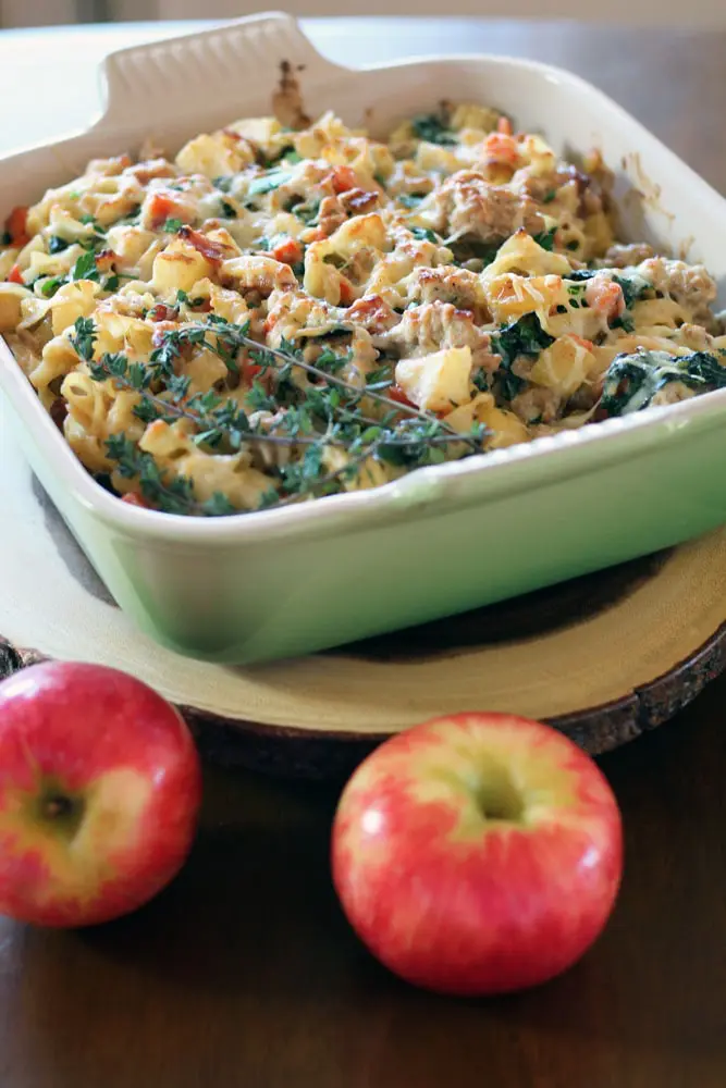 a square baking dish filled with a mixture of diced apple, pork, and spinach topped with melted cheese